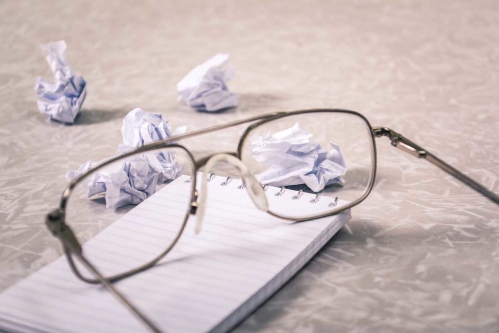 A pair of glasses alongside scrunched up paper