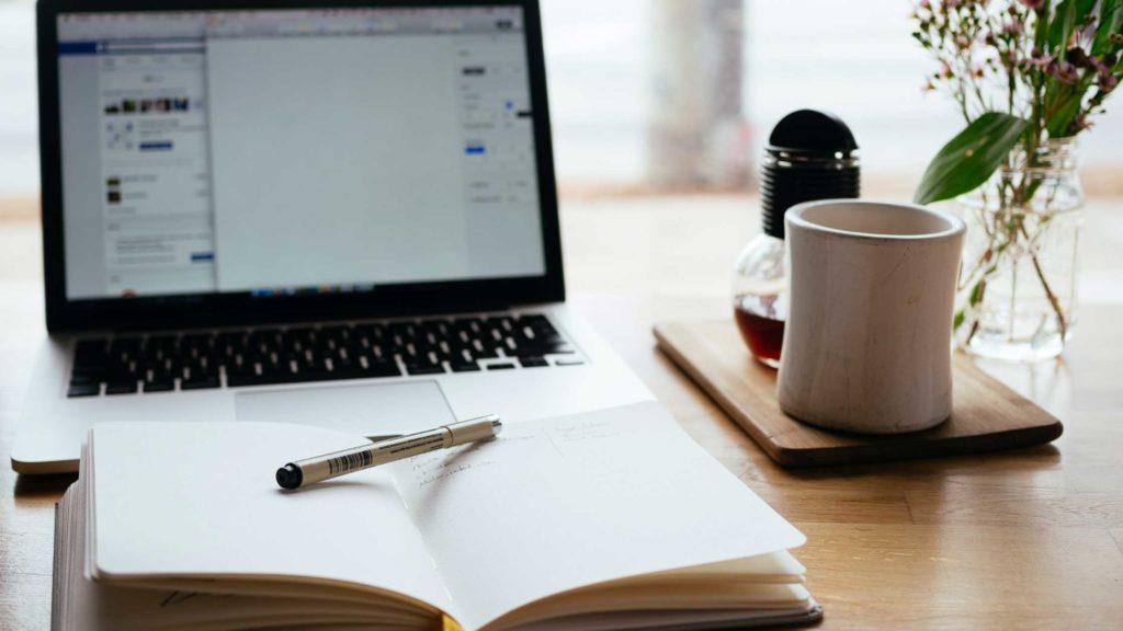 A notepad and laptop at a desk - Essential skills every copywriter must have