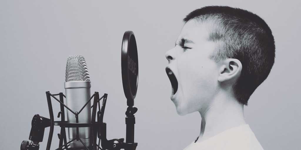 Shows a boy shouting at a microphone
