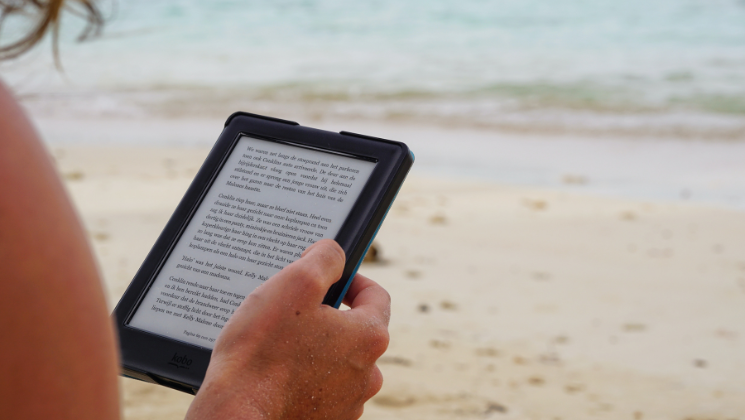 shows an image of someone reading a Kindle on the beach