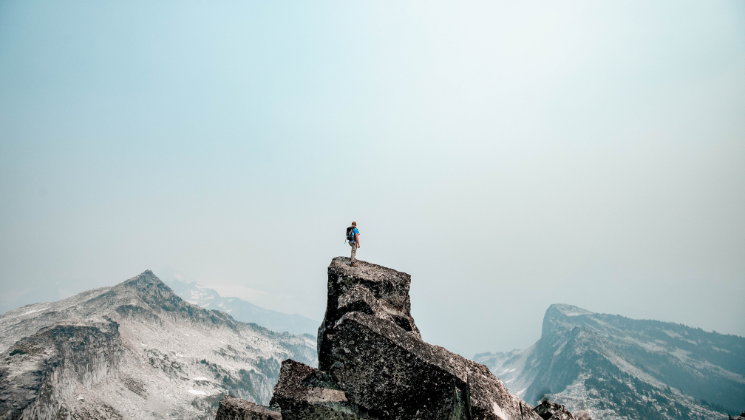 shows an inspirational image of a man standing on a mountain peak 