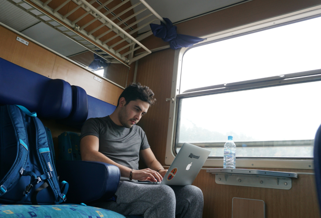 Shows a man sitting on a train writing a travel blog post