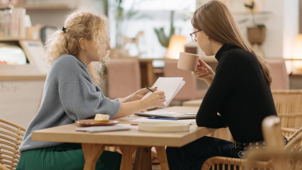 shows two women talking to eachother over a cup of coffee