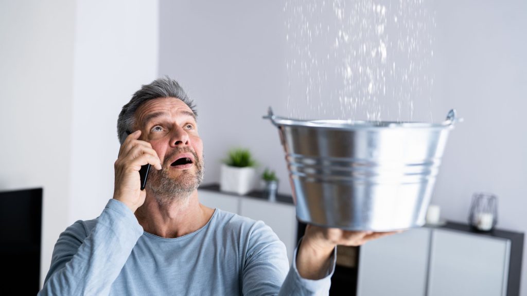 Shows a man holding a silver bucket to catch water