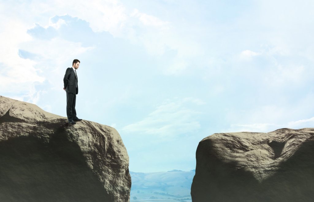 Shows a businessman in a suit looking at a gap between a gorge